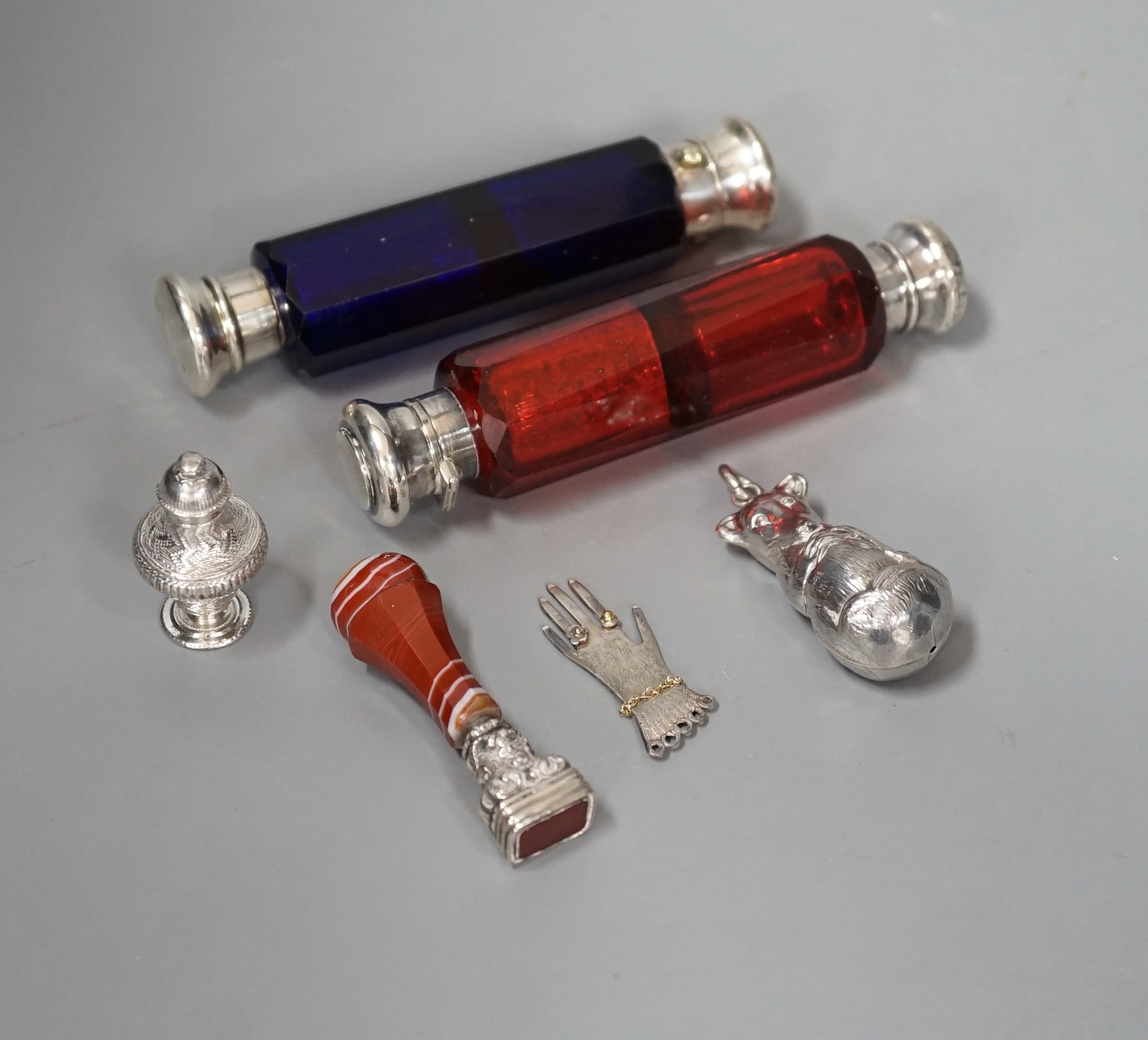 Two Victorian white metal mounted ruby or blue glass double ended scent bottles, 12.5cm, an agate mounted seal, a modern silver child's rattle, a continental scent/seal and a silver hand charm.